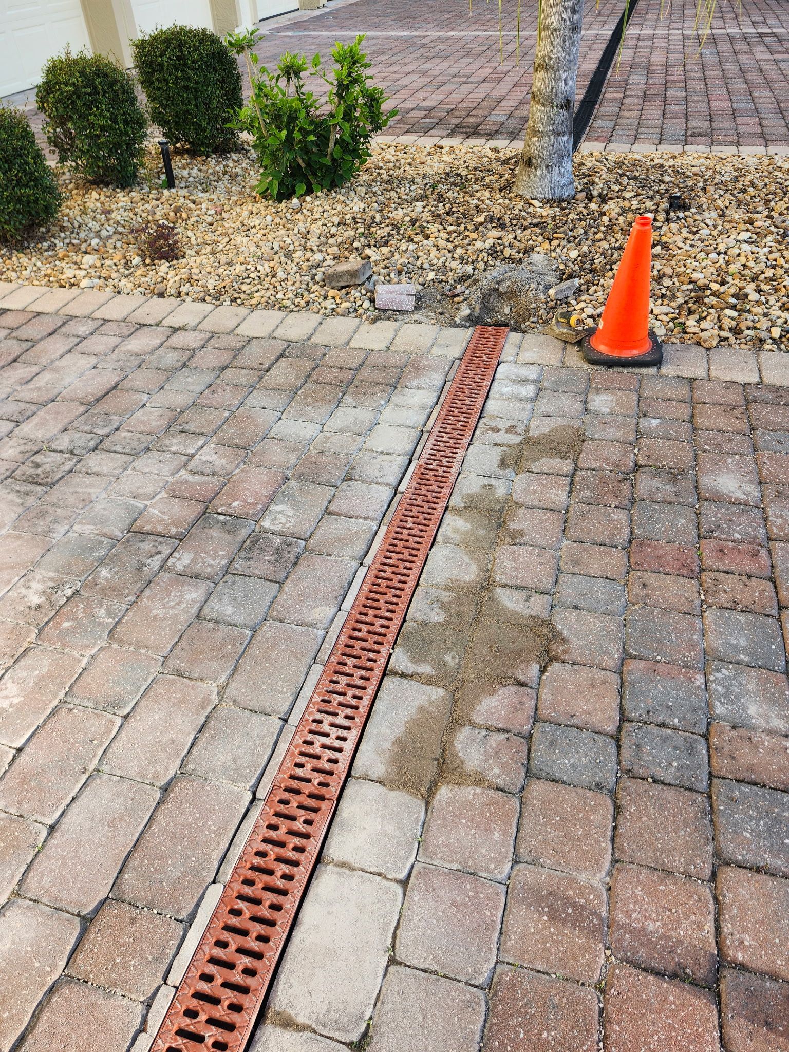 Brick paved driveway with drainage grate and orange cone.