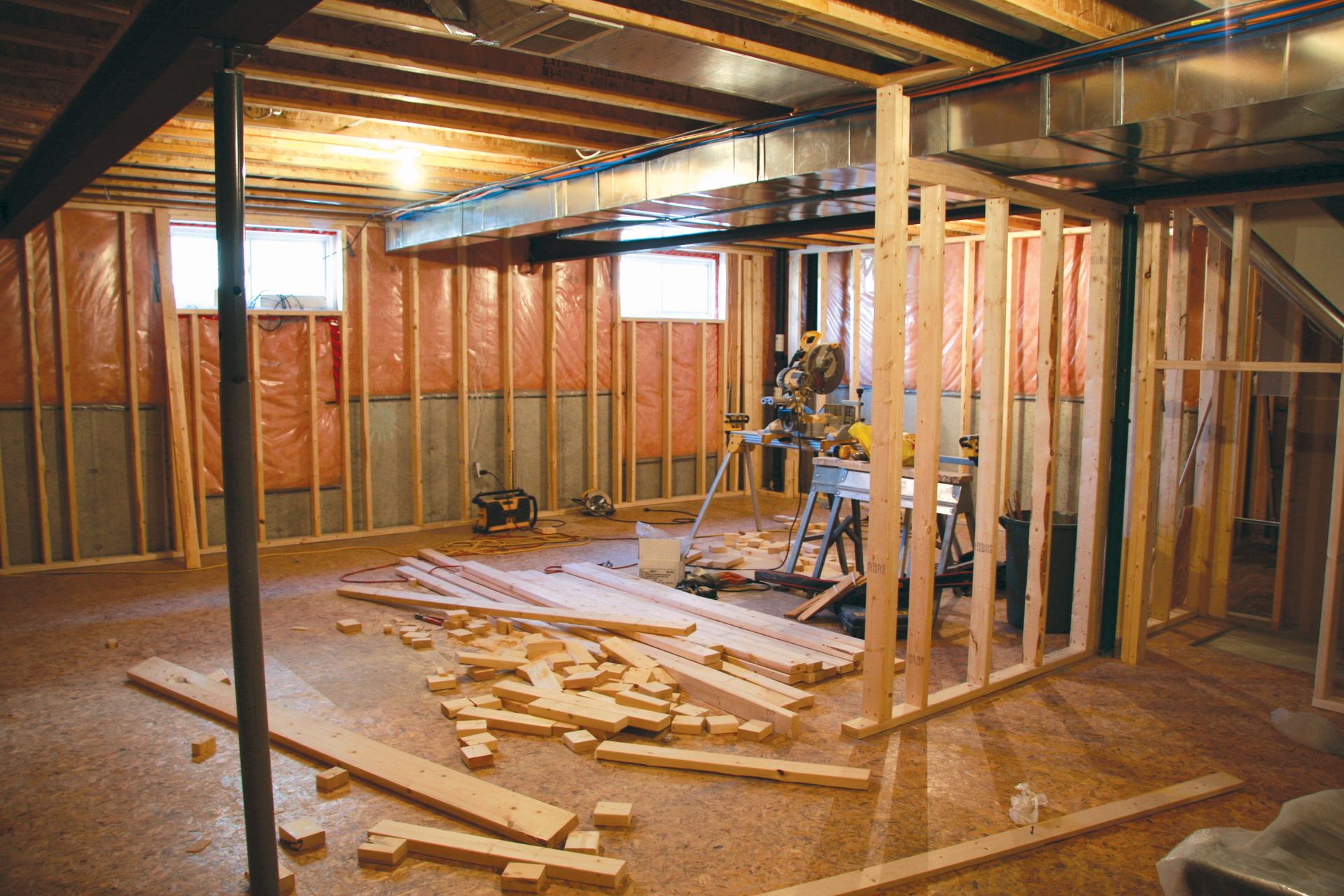 Basement remodel in progress, framed walls, insulation, exposed ceiling, tools and lumber scattered.
