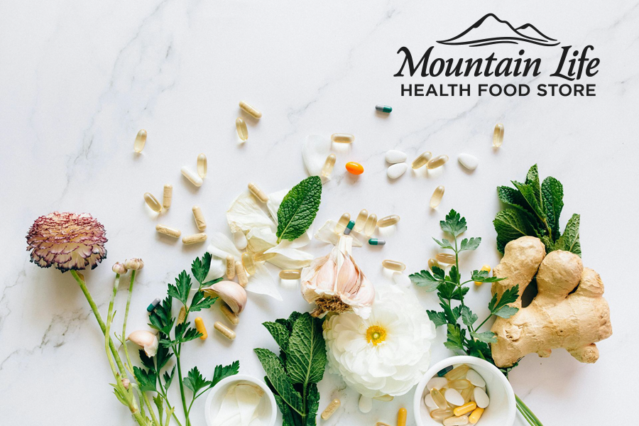 Vitamins and herbs arranged on white marble: flower, garlic, ginger, and small bowls.