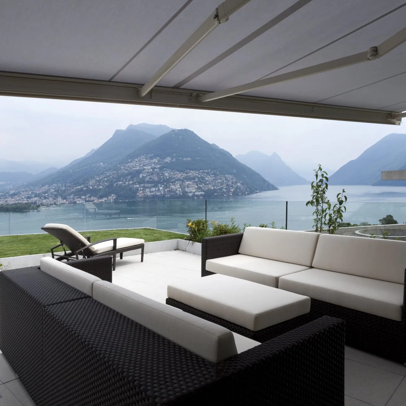 Cane and fabric outdoor setting on patio overlooking water and mountains, framed by overhead retractable awning.