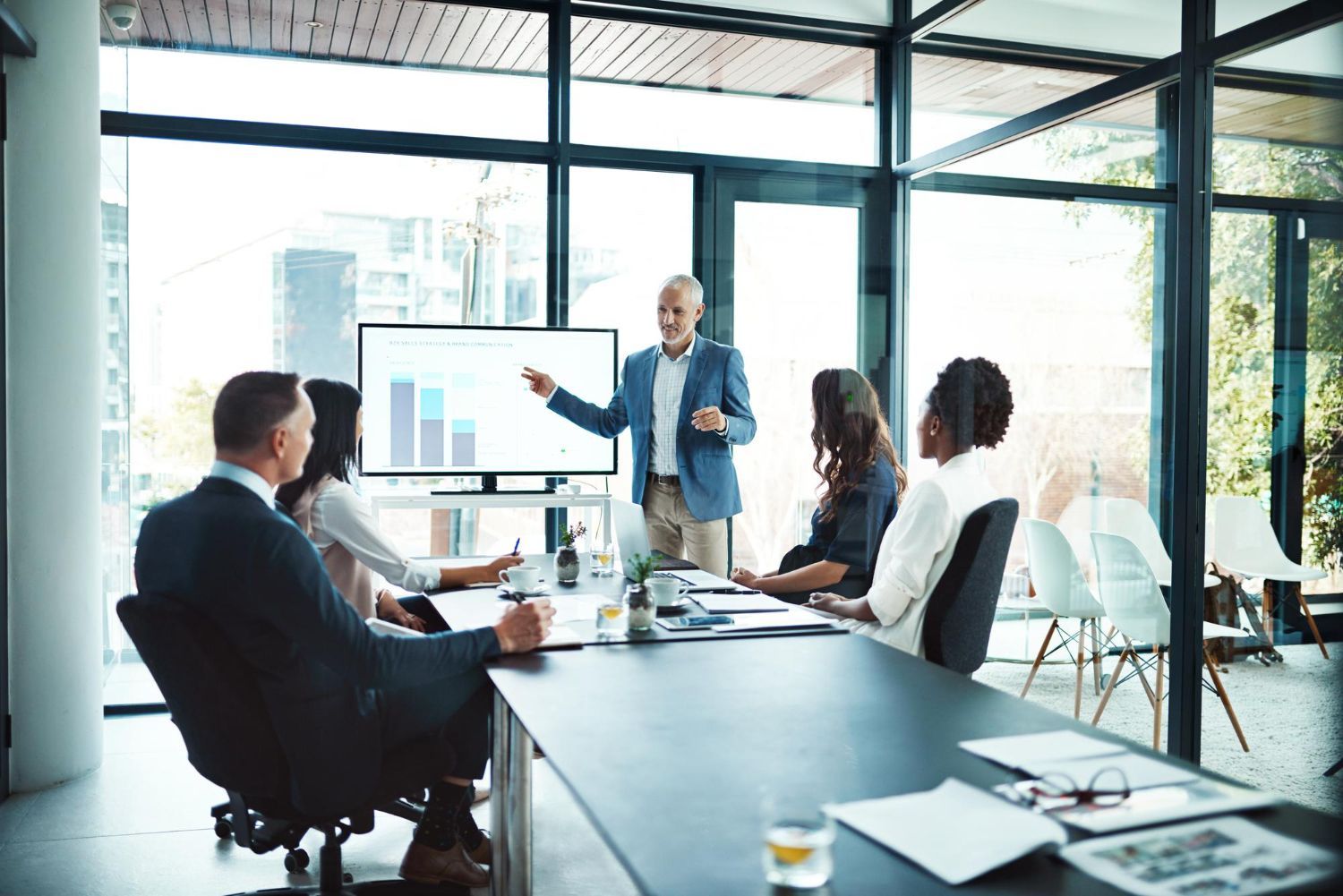 Business meeting in a bright conference room, with a presenter pointing at a chart on a screen