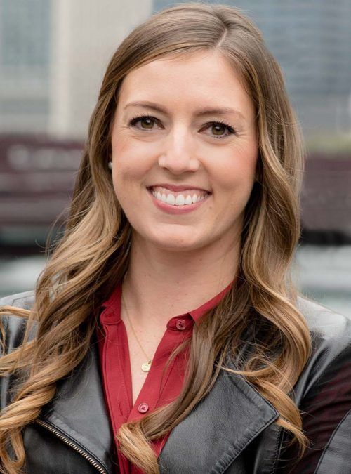 Smiling woman with long hair in a red shirt and black jacket outdoors
