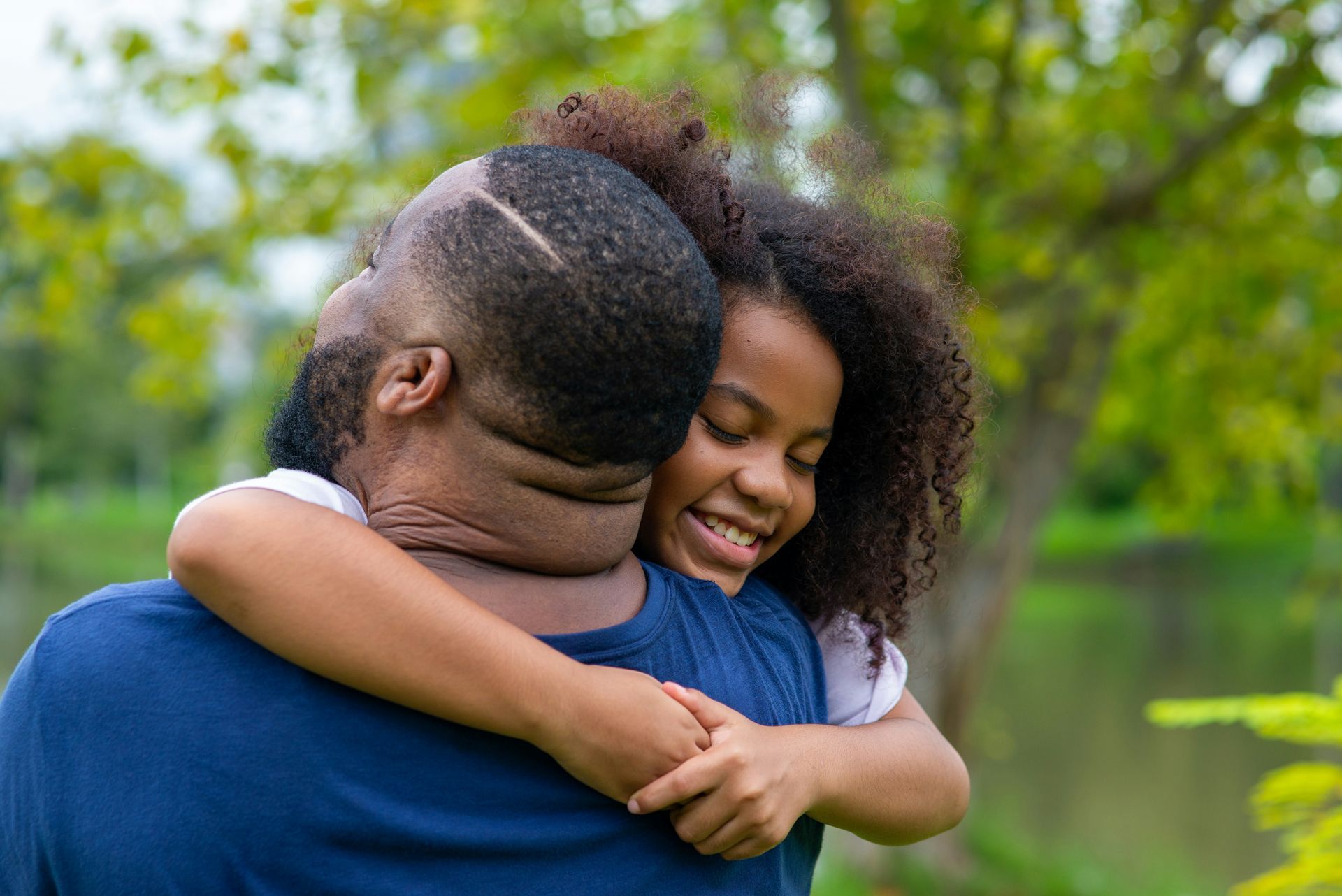 Two people hugging outdoors, smiling in a green park.