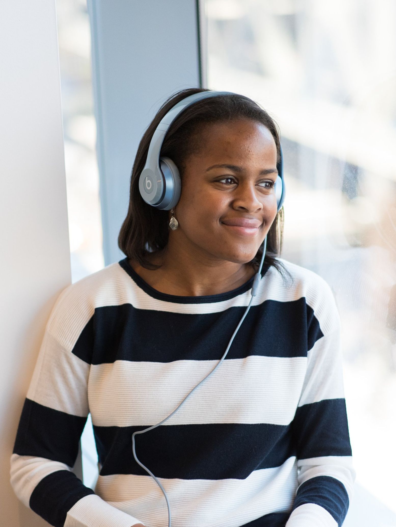 Person wearing headphones and a black-and-white striped shirt, looking out a window with a slight smile