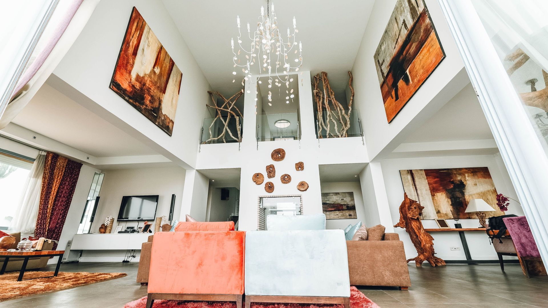 Bright modern living room with high ceilings, white walls, orange sofas, and large abstract paintings.