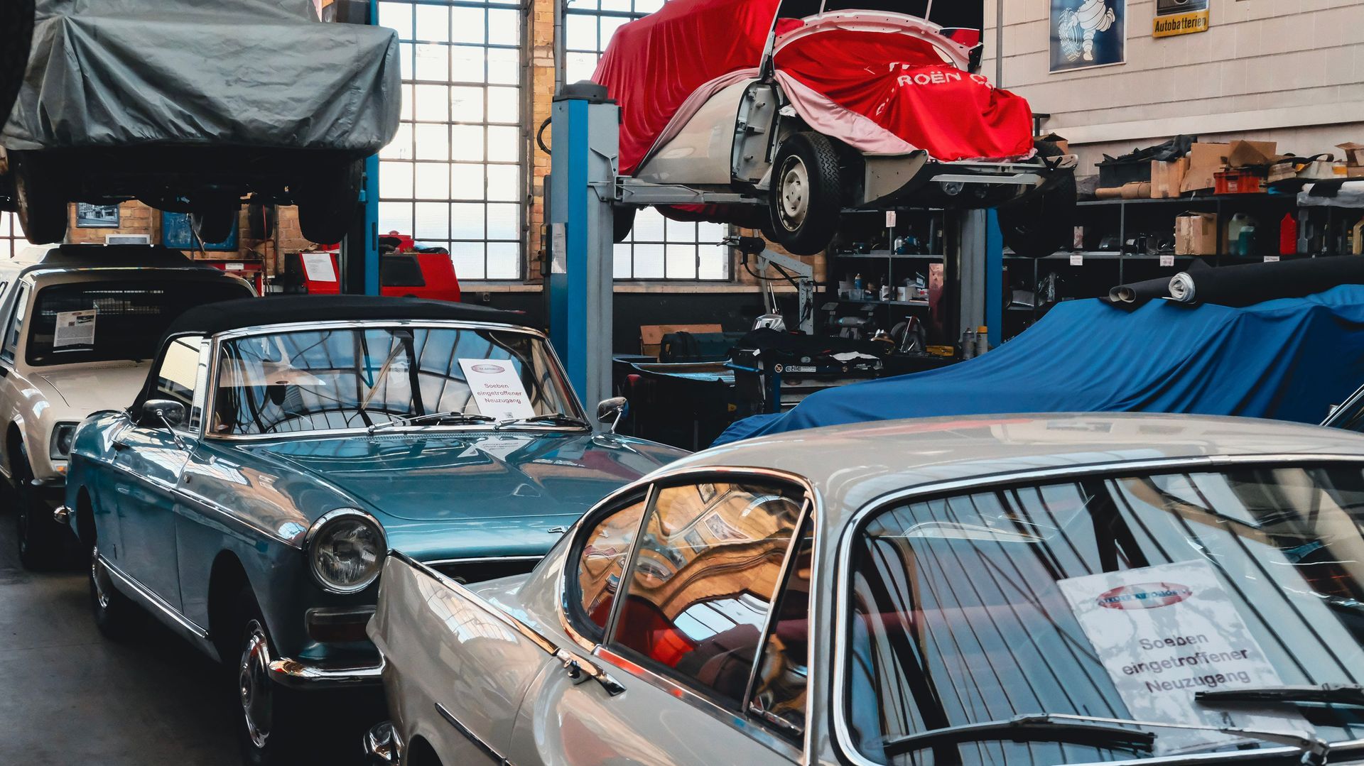 Classic cars in a workshop, with a blue convertible and white coupe under repair lifts