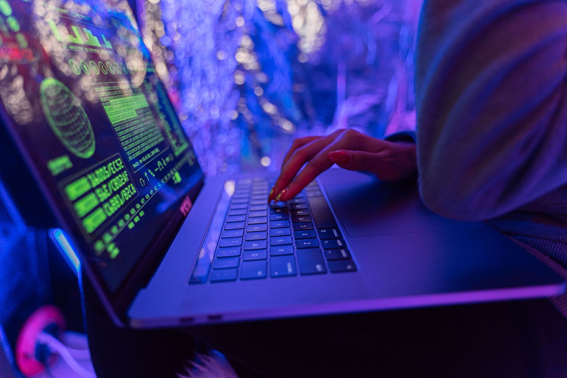 Person typing on a laptop with neon green code in a purple-lit room
