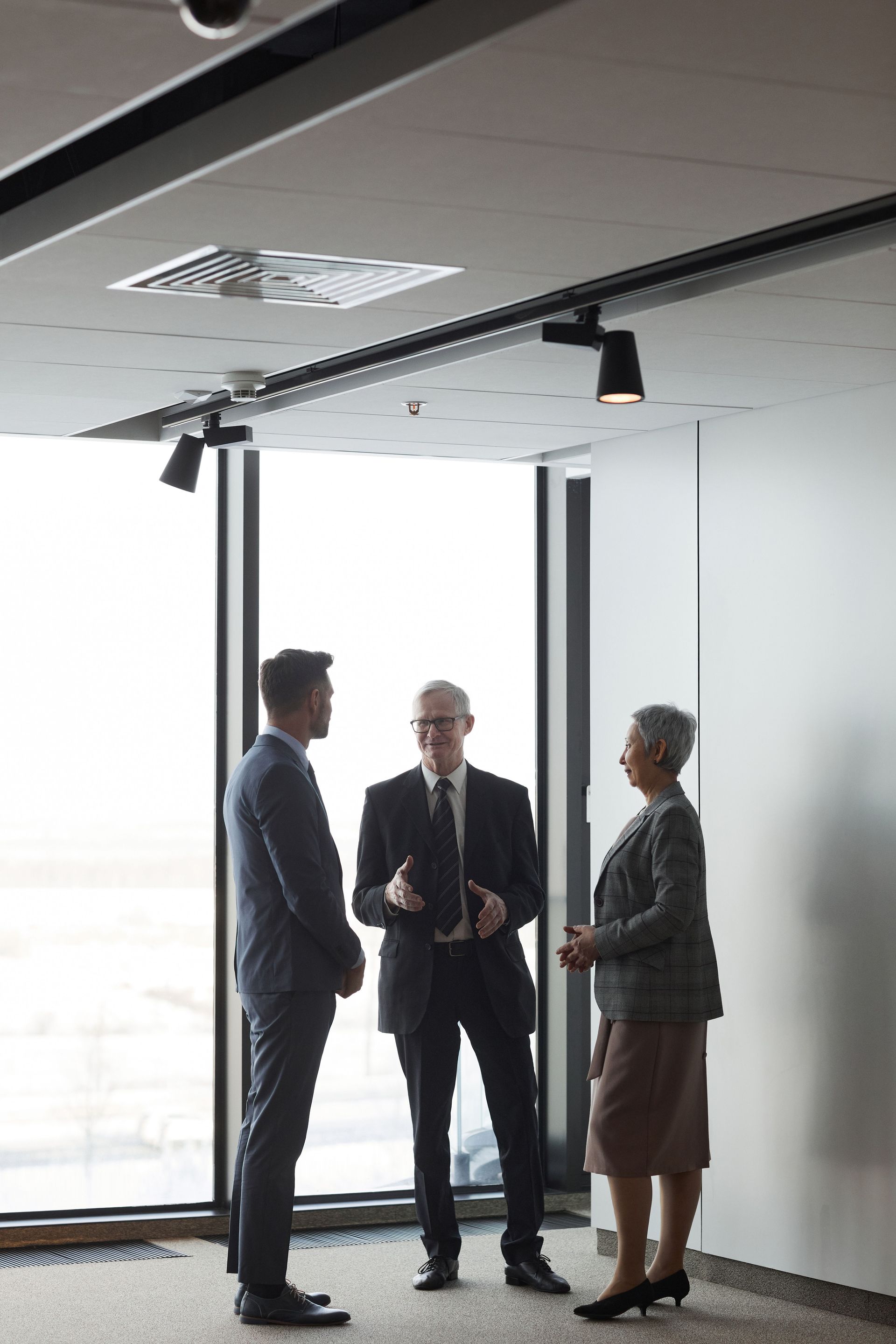 Three people talking in a bright office near large windows