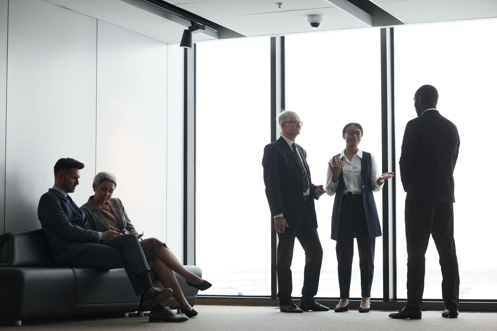 People standing and talking in a bright modern office lobby, with two seated on a couch.