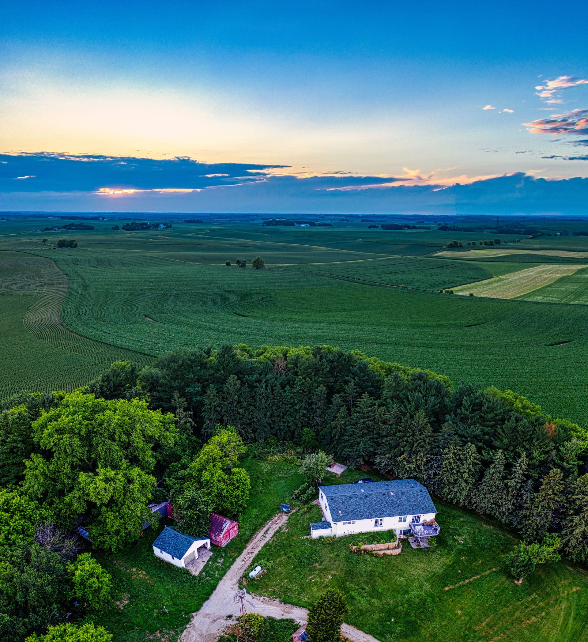 Aerial view of a rural farmhouse and dirt road beside green fields at sunset