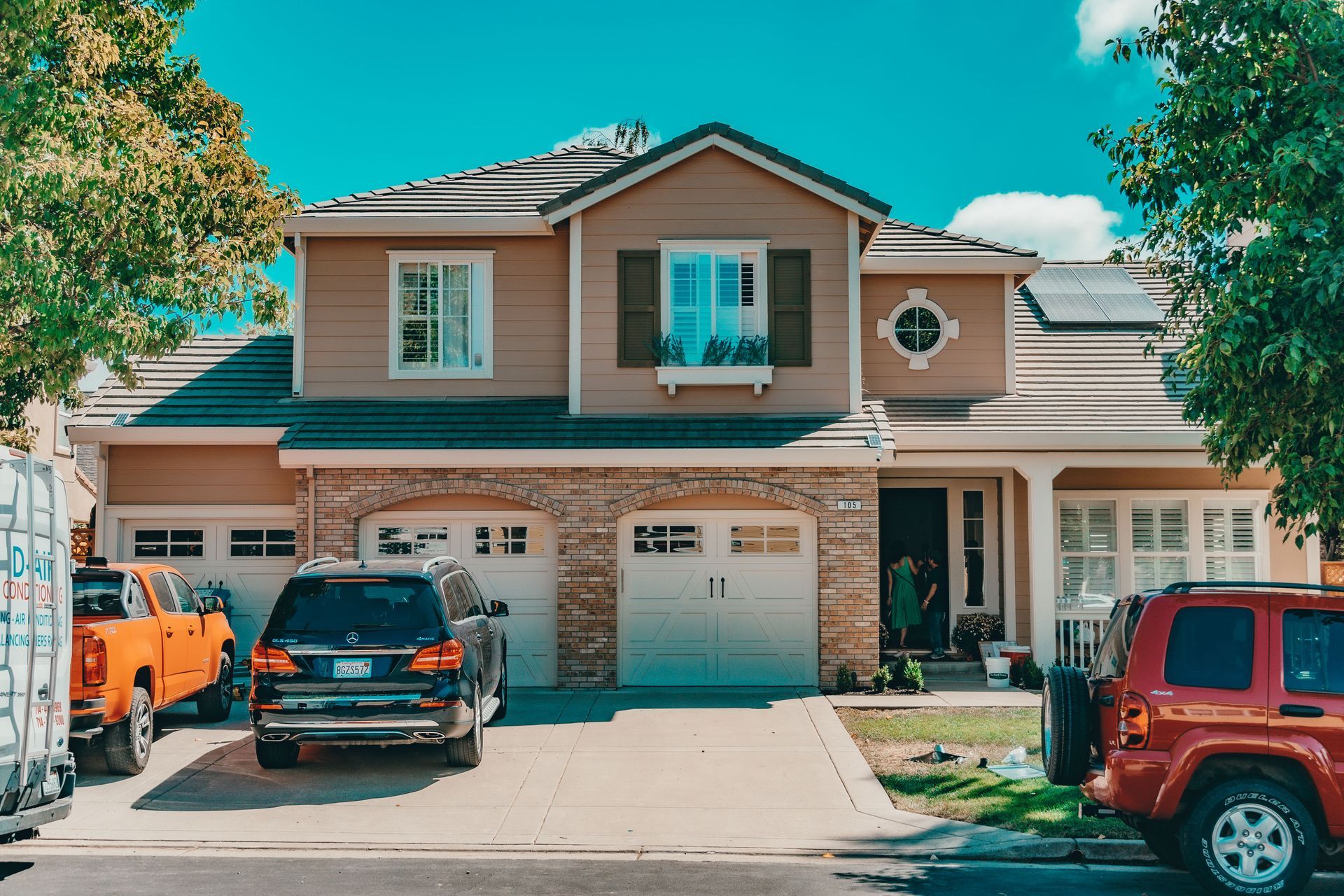 Suburban two-story house with three cars parked in the driveway on a sunny day