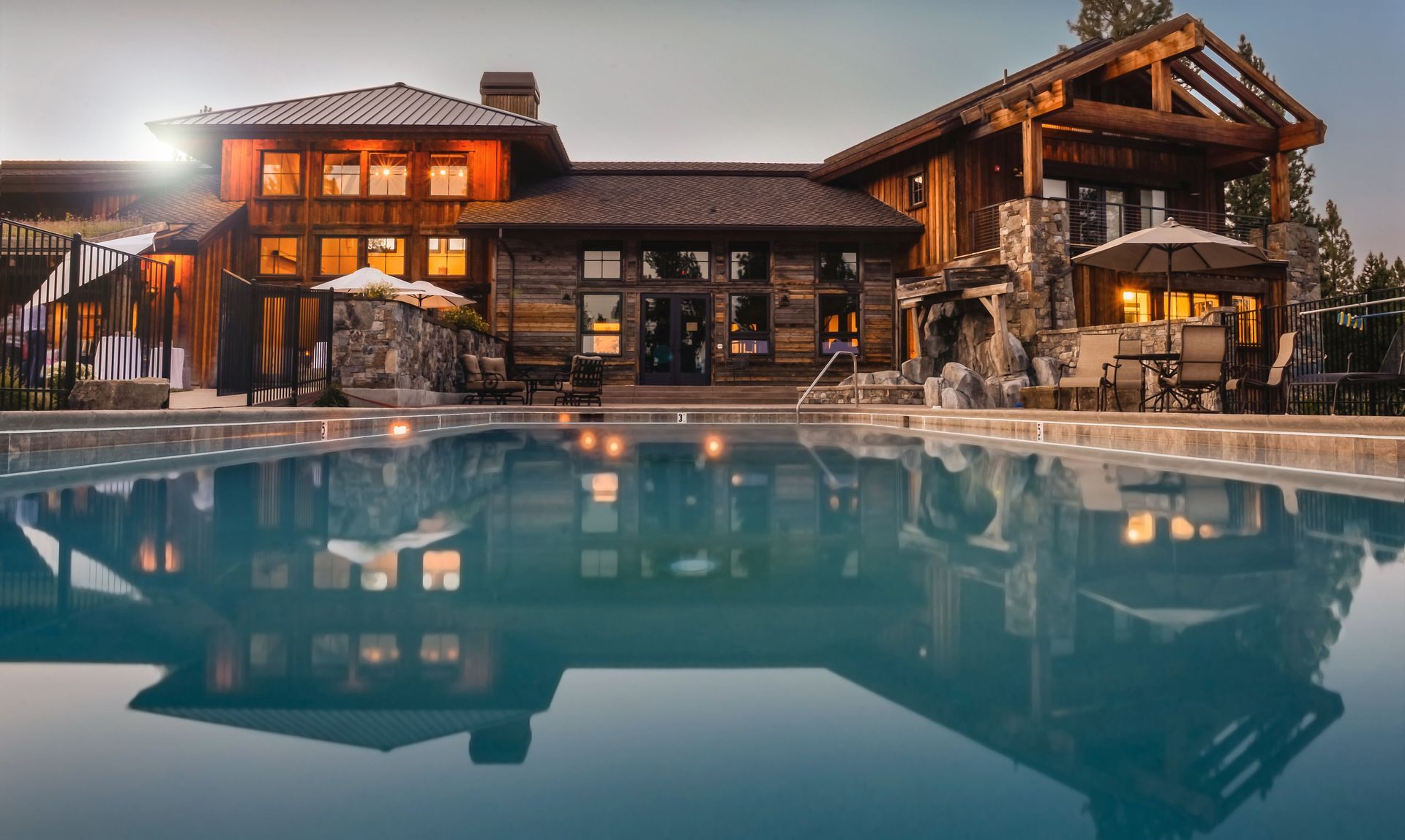 Luxury lodge with warm lights reflected in a calm outdoor pool at dusk
