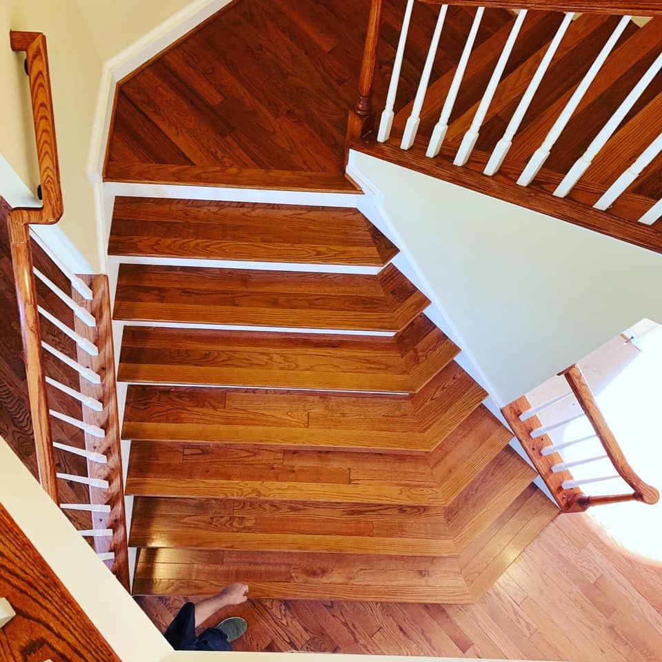 A top-down view of wooden stairs with white spindles and a handrail, descending to a landing.