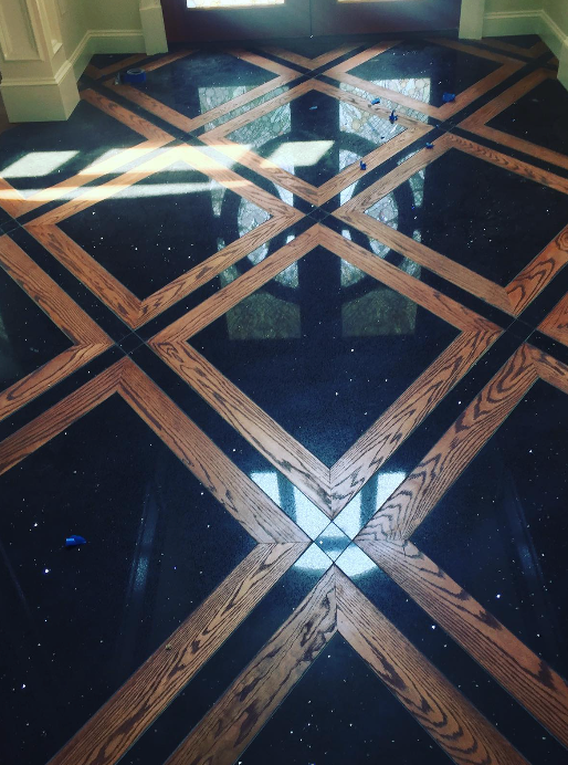 An entryway floor featuring a geometric pattern of dark, speckled tiles inlaid with light wood borders.