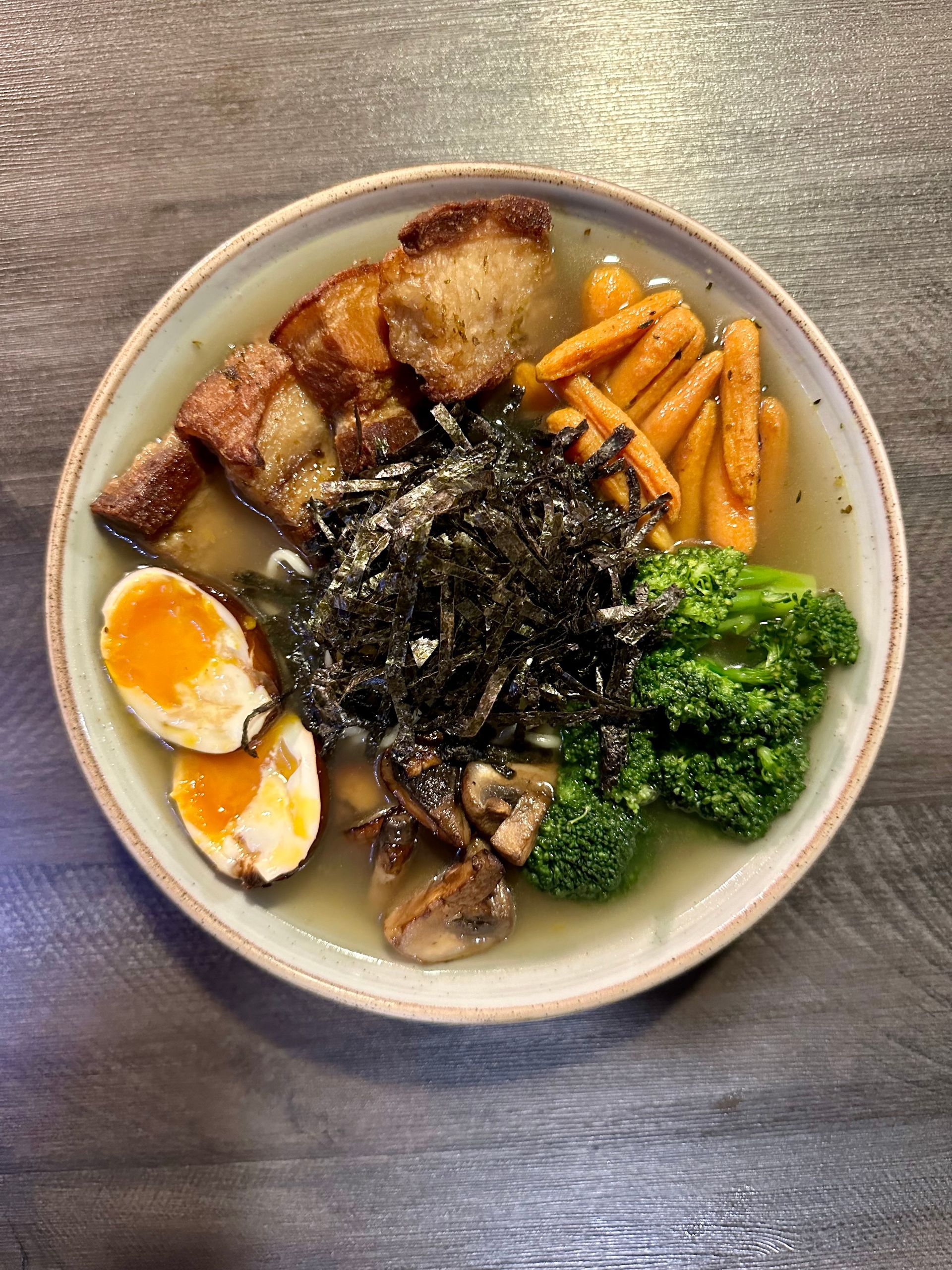 Un plato de ramen con brócoli, zanahorias, huevos y algas sobre una mesa menu asiatico  hotel Lagoon Llanogrande.