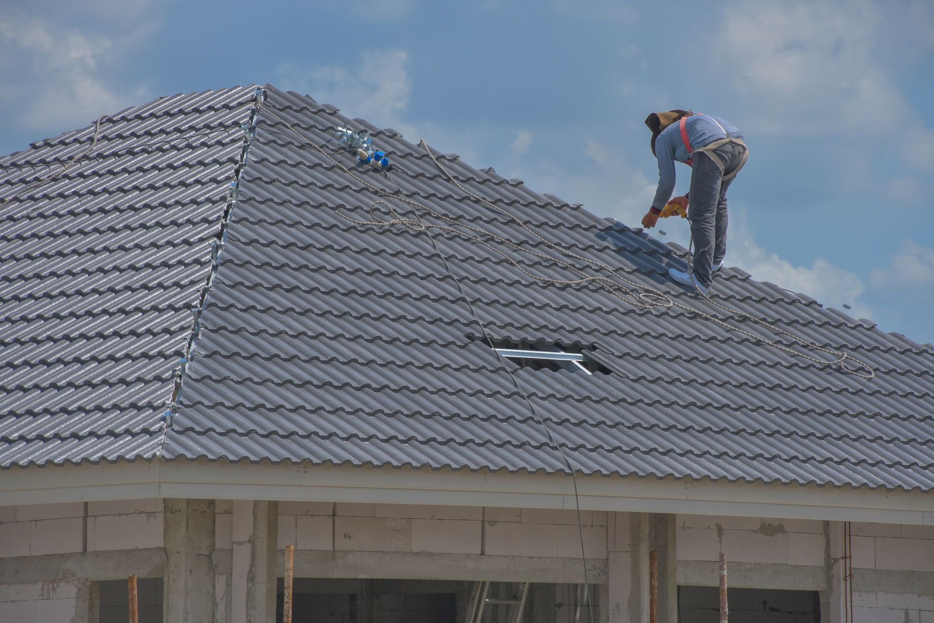 Roofer working on a gray tiled roof of a building under construction, blue sky in the background.