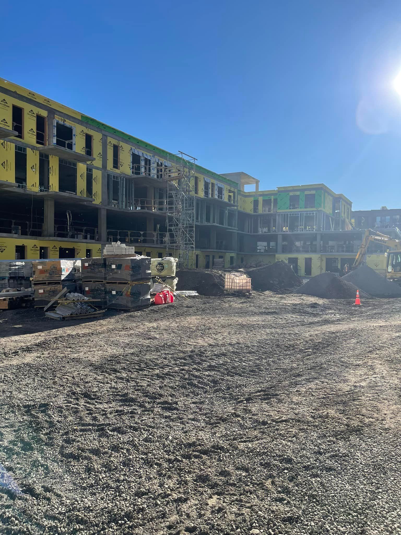A multi-story commercial building under construction with exposed wooden framing and yellow sheathing on a gravel lot.