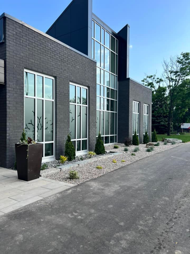 A modern building with dark brick walls, tall vertical windows, and a landscaped rock garden bed along a paved path.