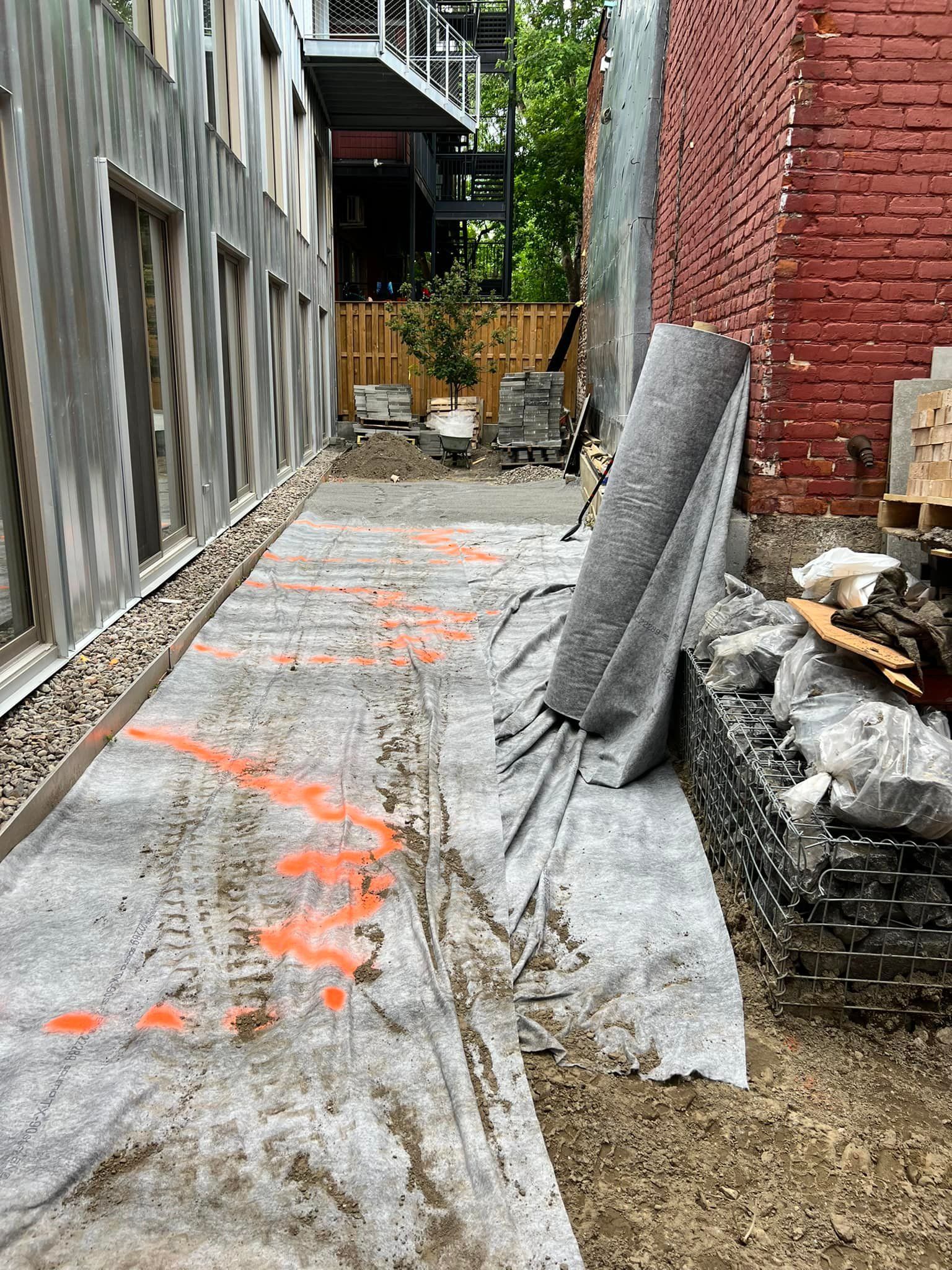 Construction site exterior featuring a path covered with protective fabric marked with orange paint next to brick walls.
