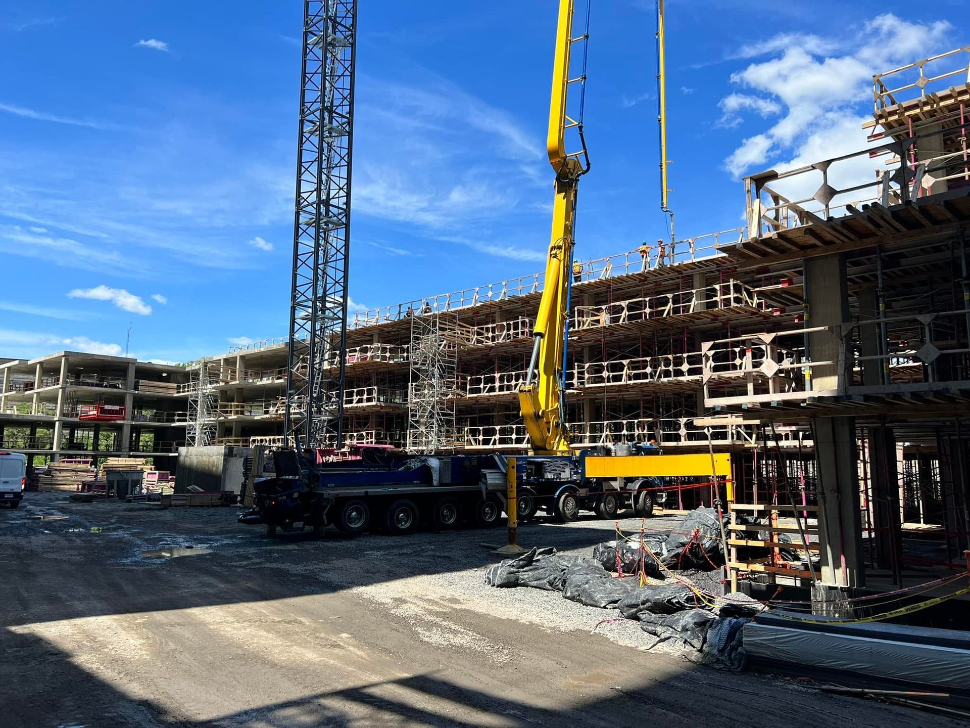 A yellow concrete boom pump truck operates at a construction site with multi-level scaffolding against a blue sky.