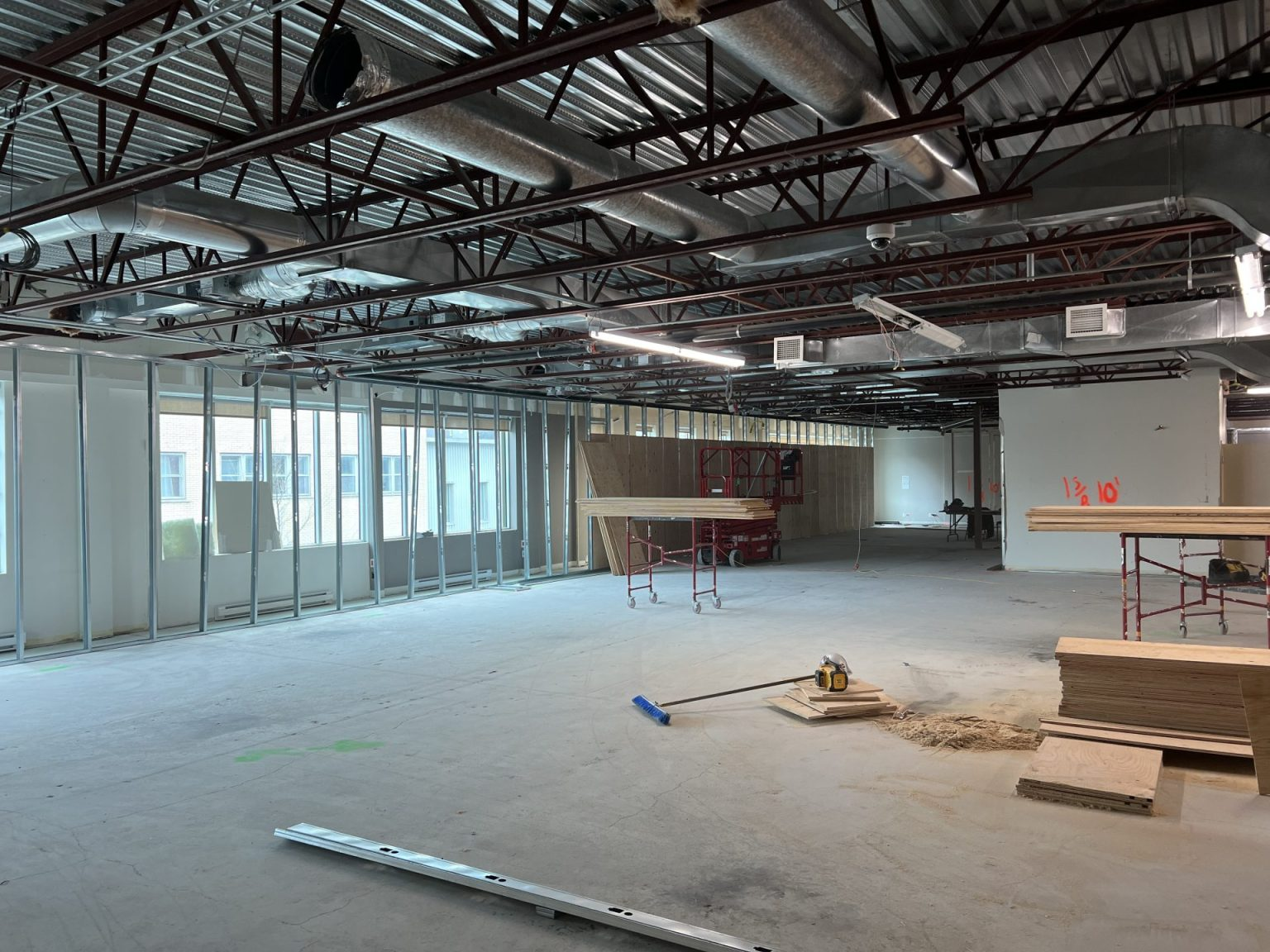 Vue intérieure d'un chantier de construction commerciale avec solives de plafond apparentes, charpente métallique et matériaux de construction.