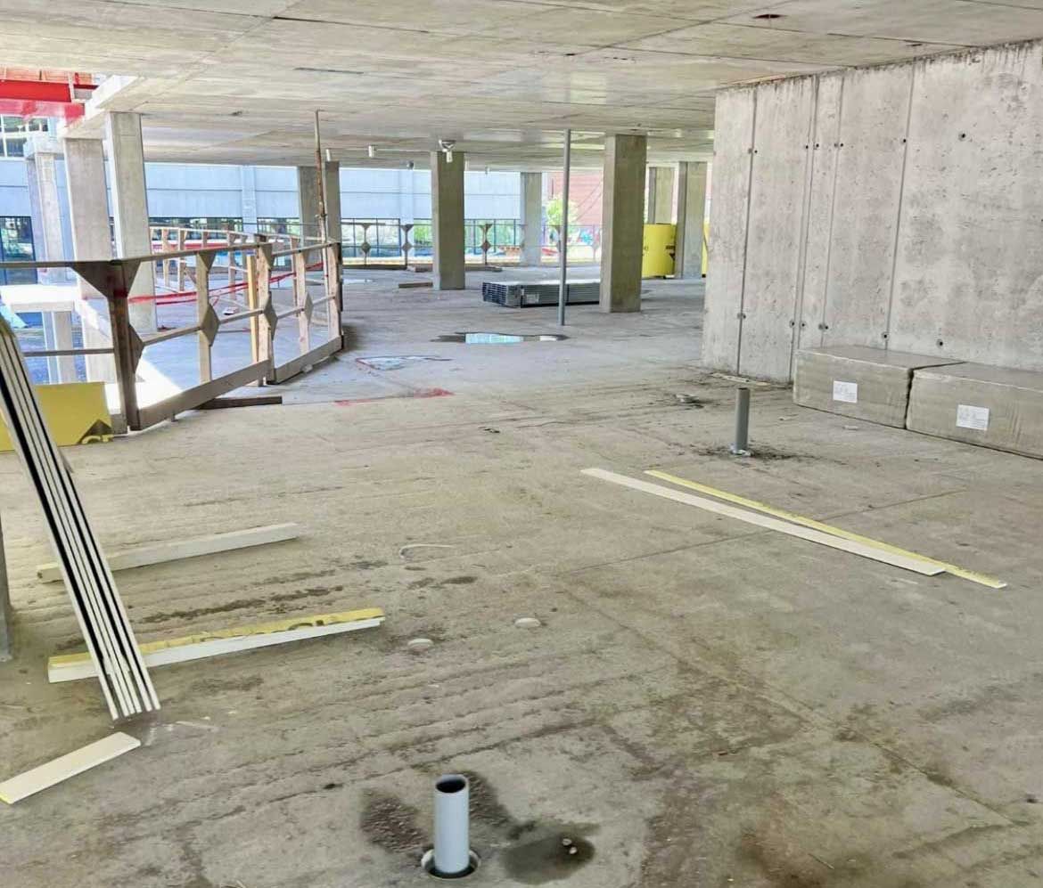 Construction site interior showing exposed concrete floors, support pillars, and scaffolding in an unfinished space.