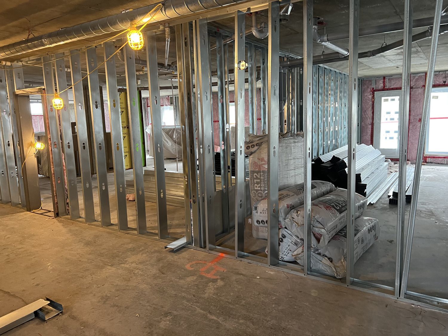 Construction interior with metal wall framing, open studs, and insulation materials on a concrete floor.