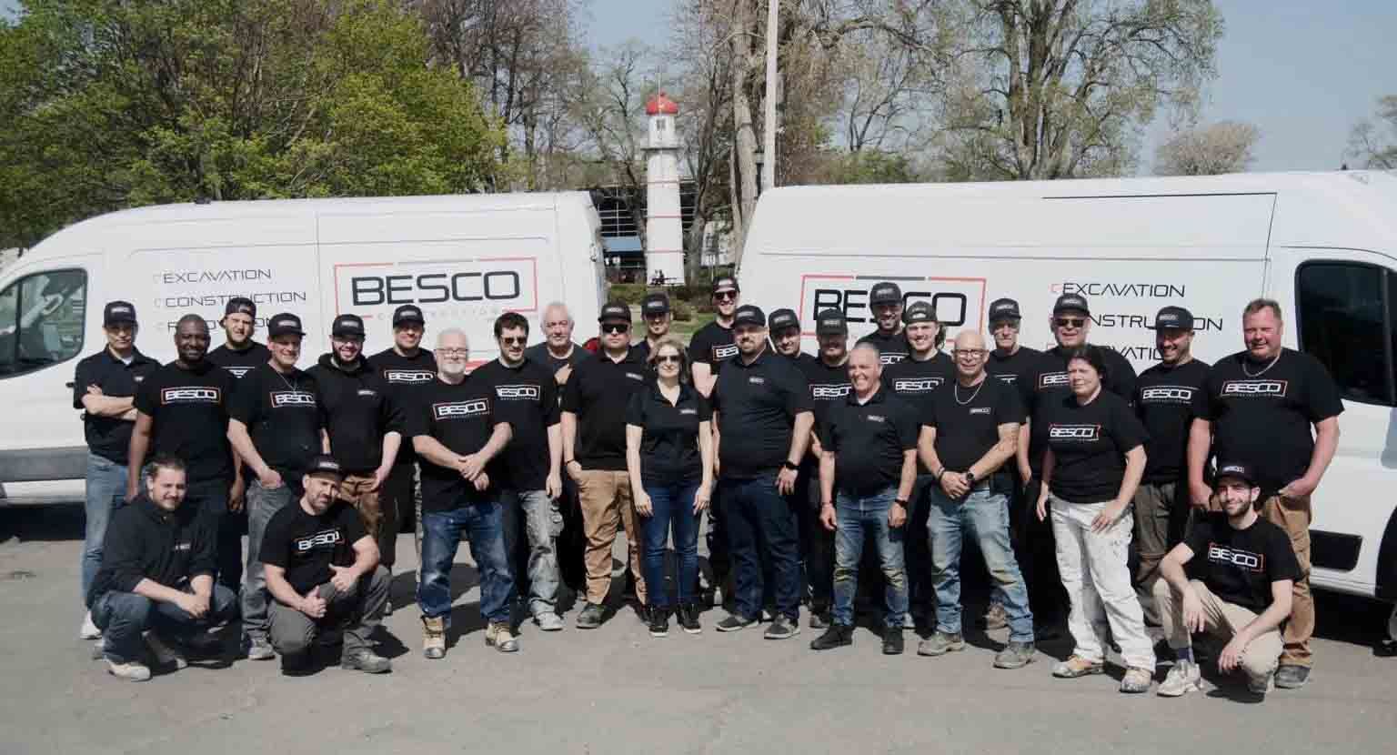 Un groupe d'employés portant des t-shirts noirs Besco pose pour une photo devant deux fourgonnettes blanches de l'entreprise, à l'extérieur.