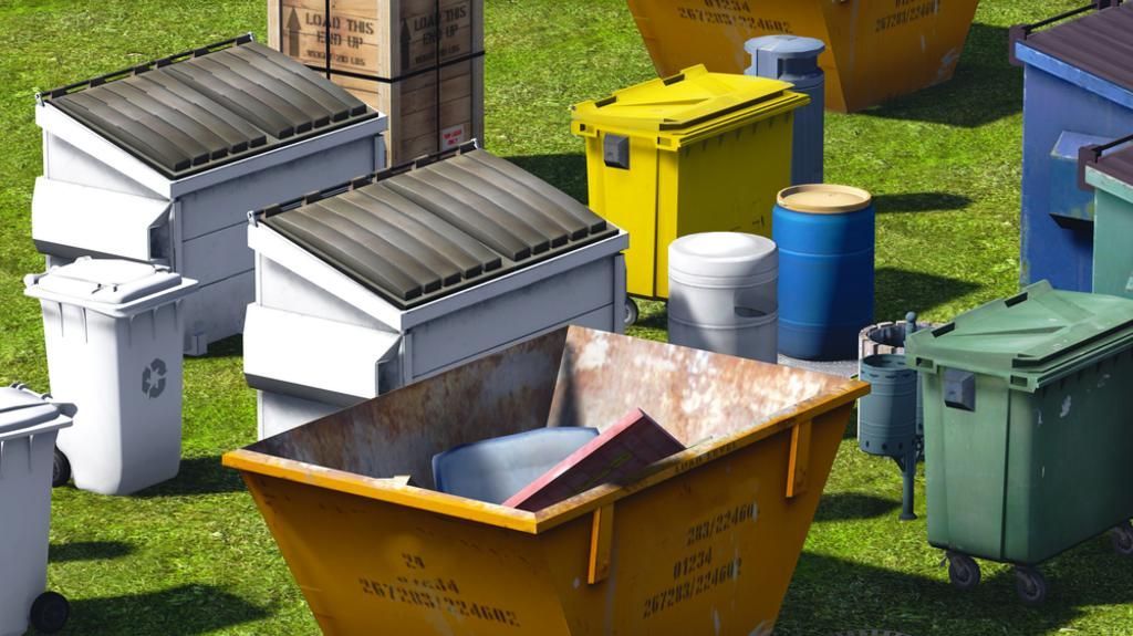 Assorted colorful trash and recycling bins lined up on grass near a brick wall