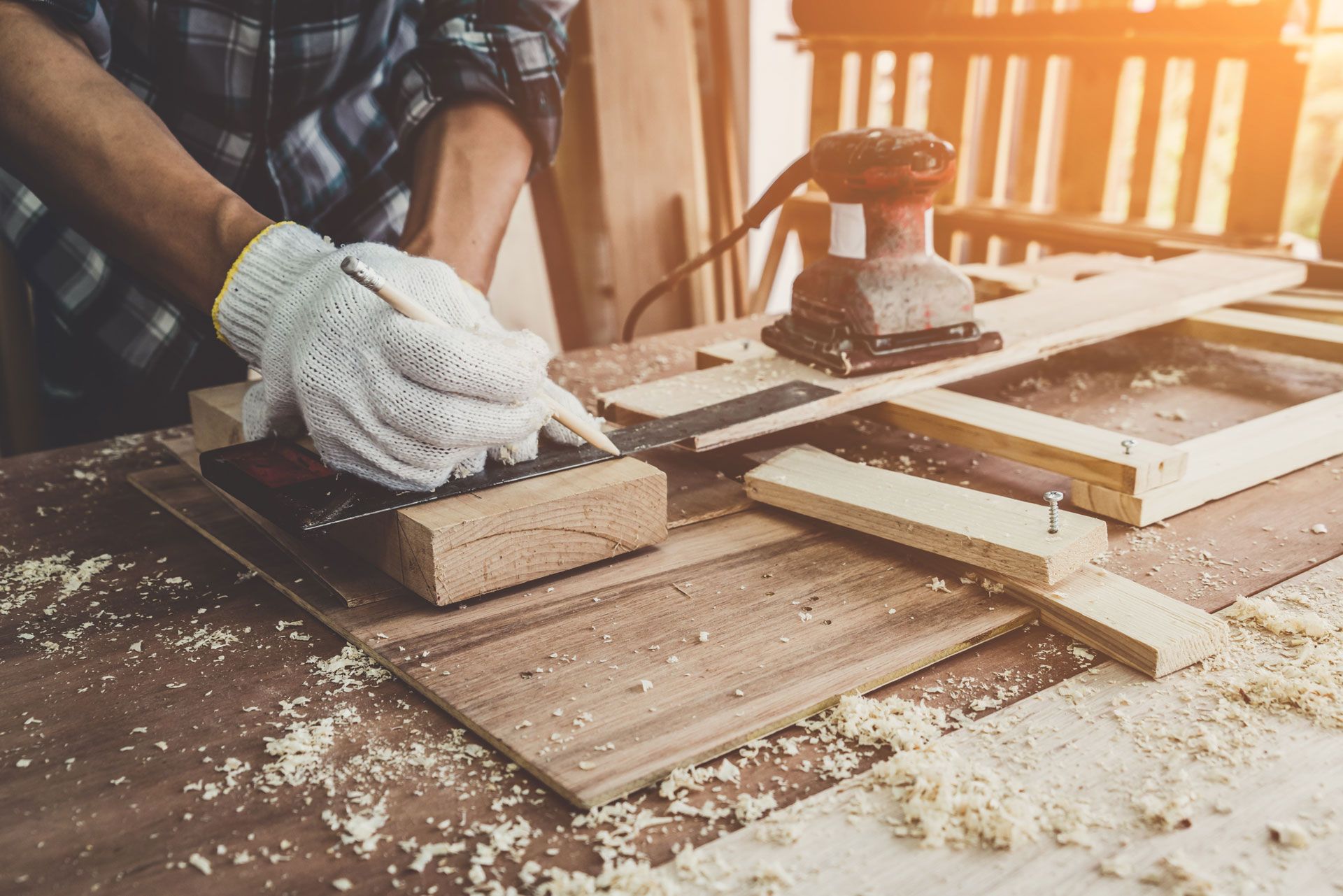 Gloved hands sanding a wooden board on a workbench in a sunlit workshop