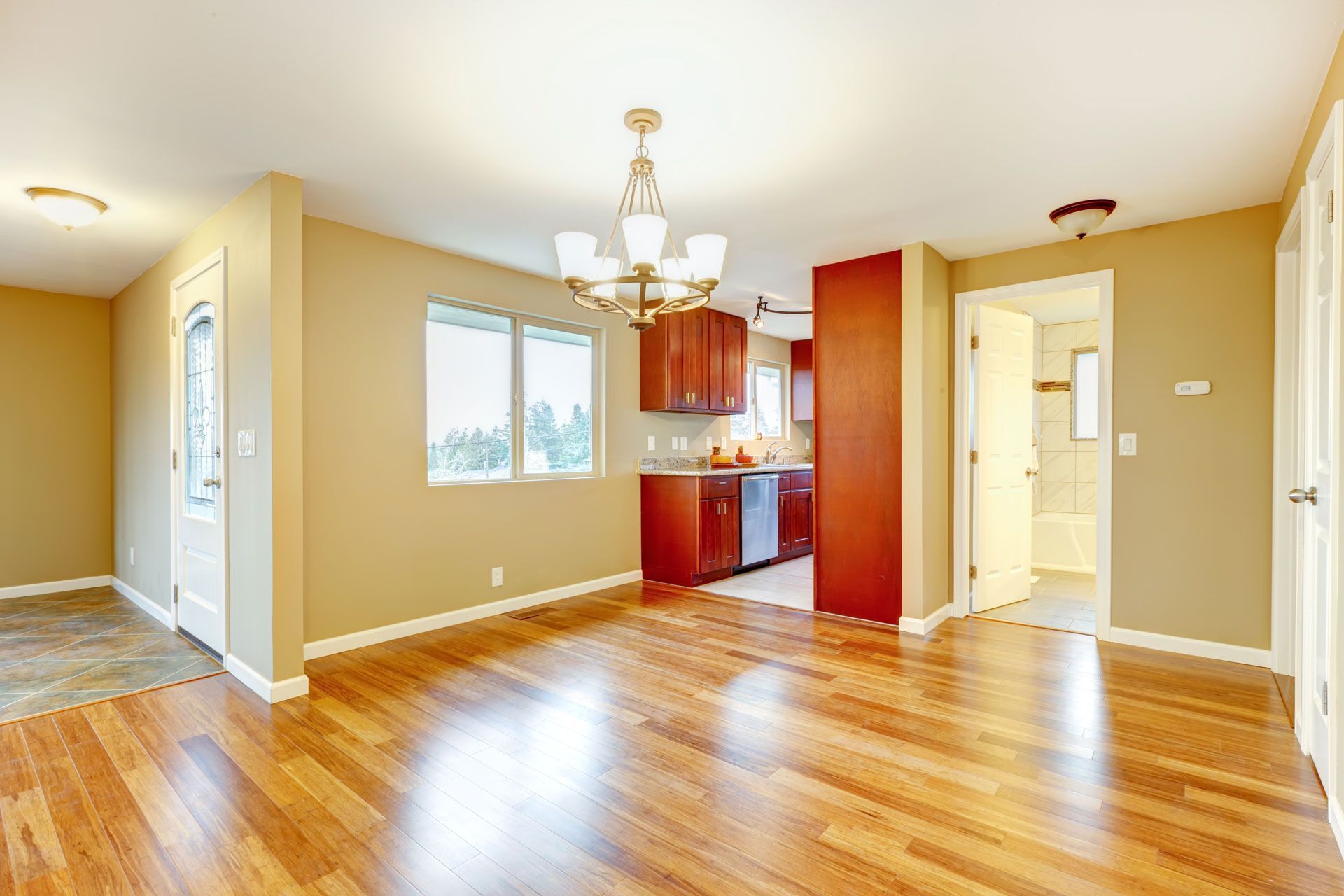 Bright empty dining room with hardwood floors, chandelier, and adjacent kitchen and hallway