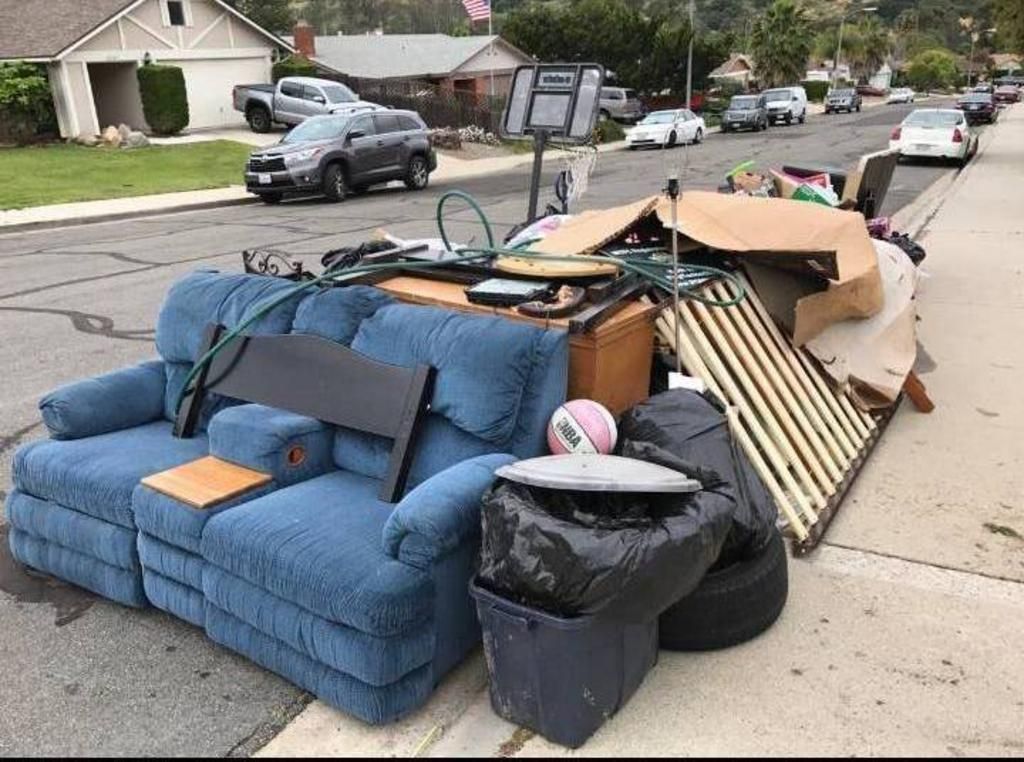 Pile of discarded furniture and cardboard piled on a residential street curb.