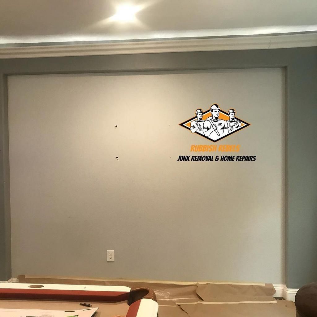 Empty gray wall with a centered logo decal above cardboard sheets on the floor.