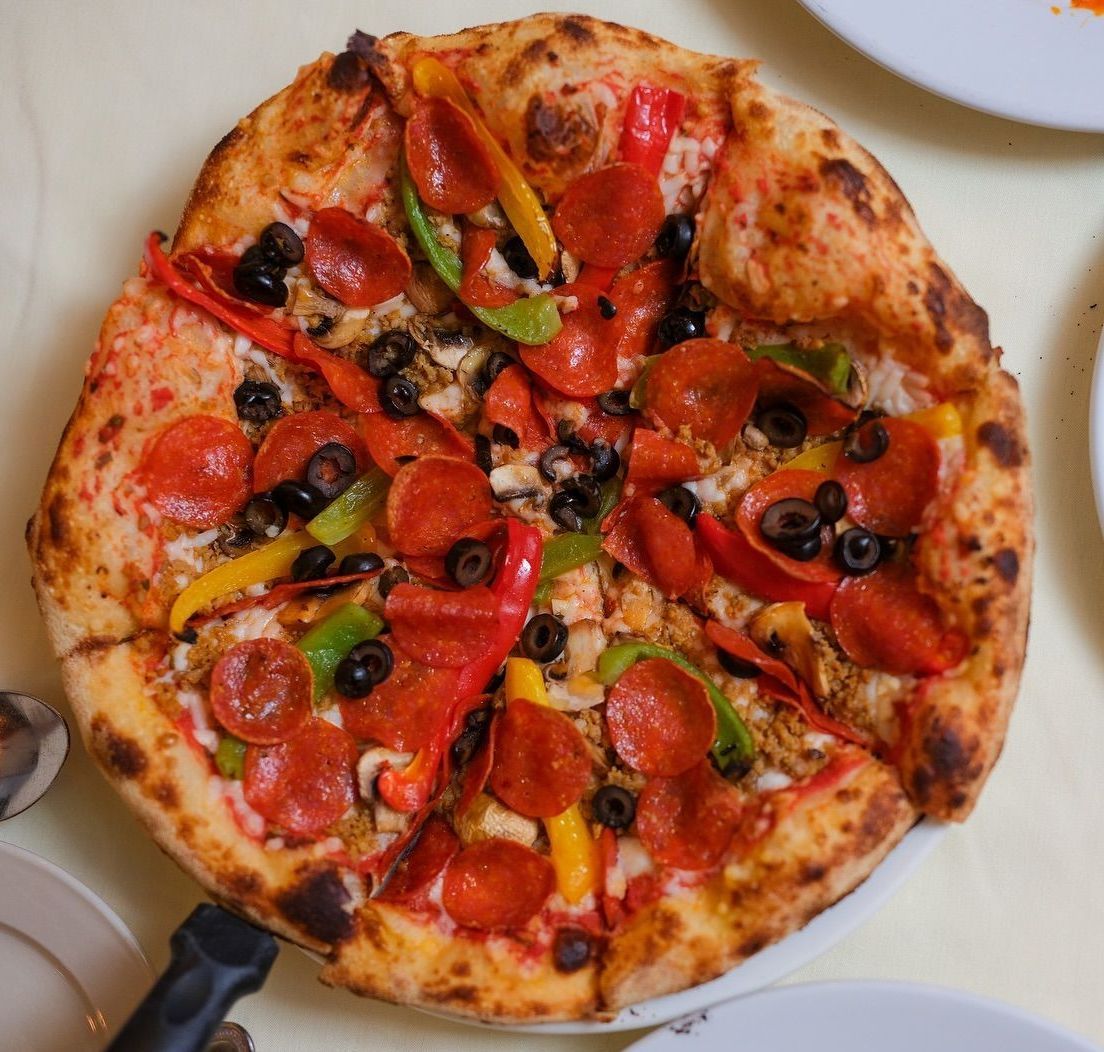A pizza with pepperoni and olives on a white plate