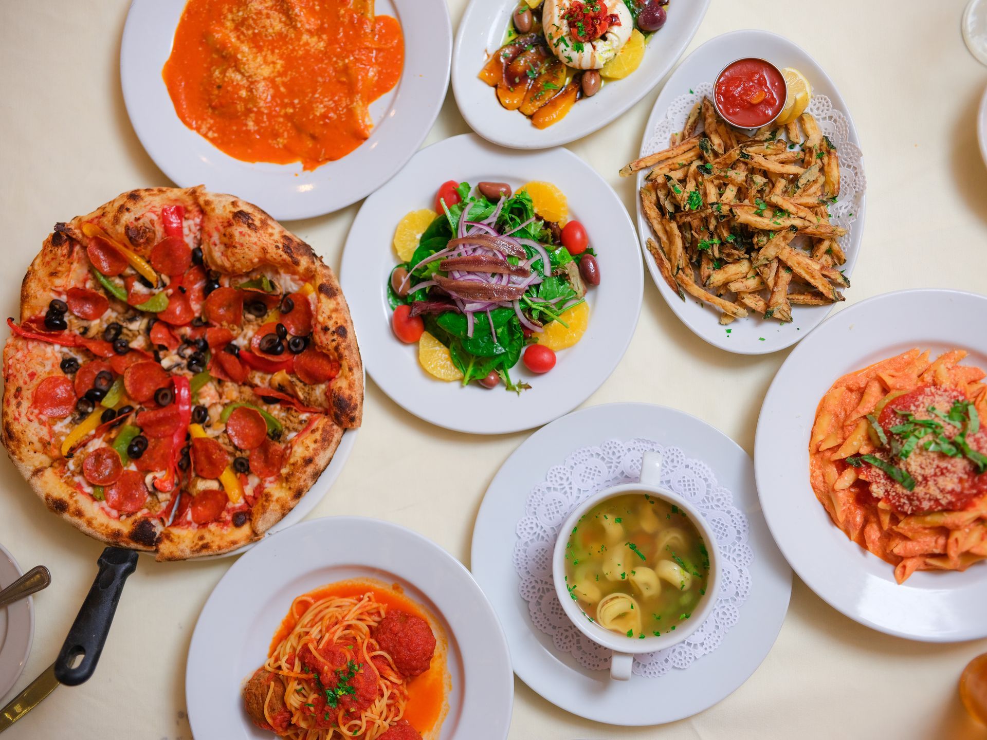 A table topped with plates of food including a pizza and a bowl of soup