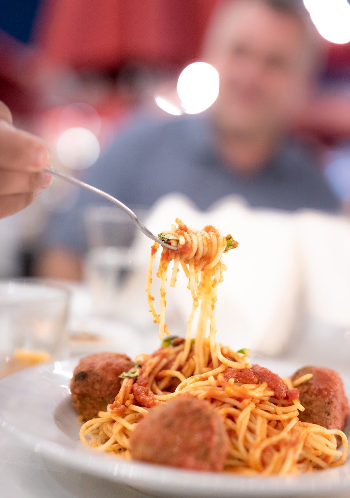 A person is eating spaghetti and meatballs with a fork.