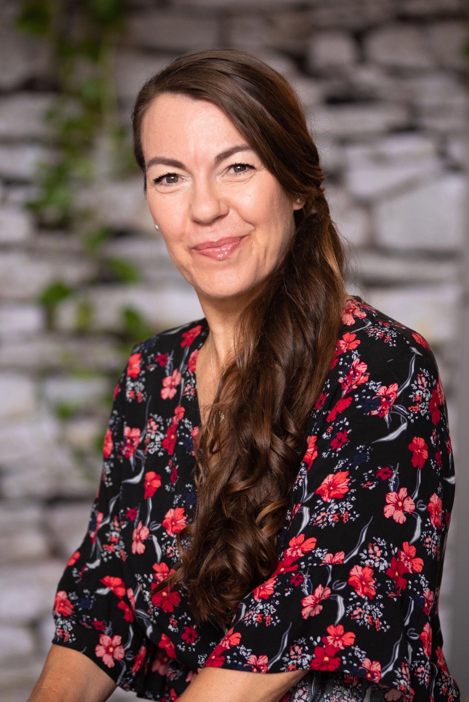 Noosa Wedding Celebrant Philippa Holness with brown hair in a ponytail wearing a dress with red flowers and smiling