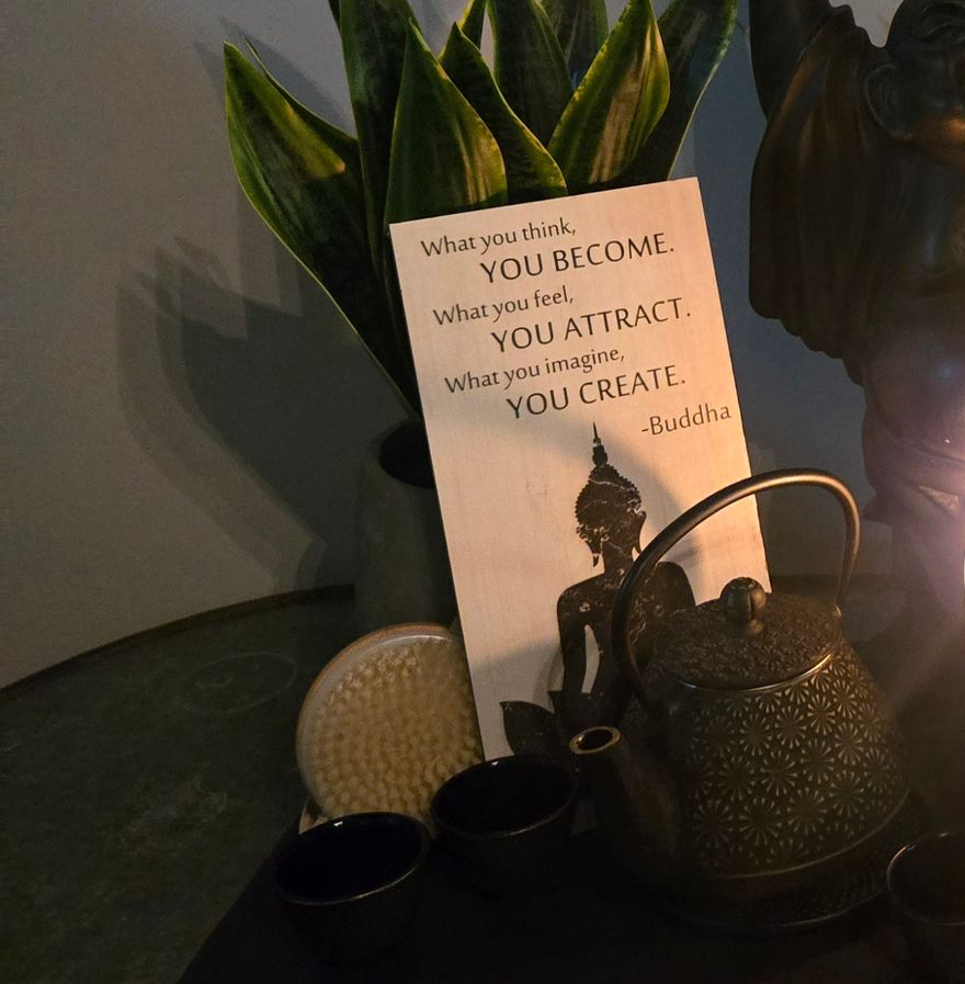 Zen-like composition: Buddha statue holding rake, candle, teapot, plants, book, towels, on a dark surface.