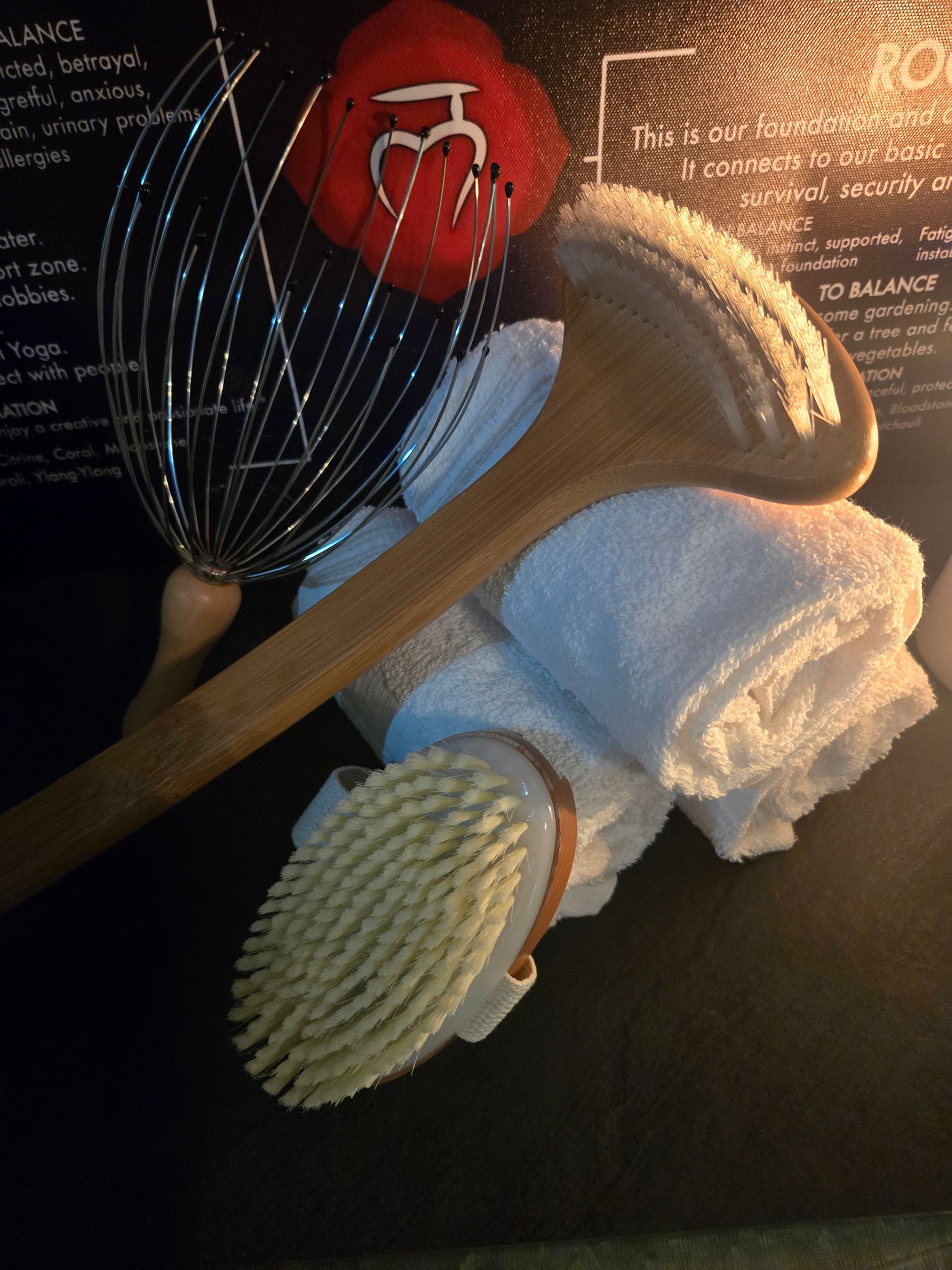 Assorted spa items on a dark surface: wooden spoon, brush, towel, strainer, and a red pouch.