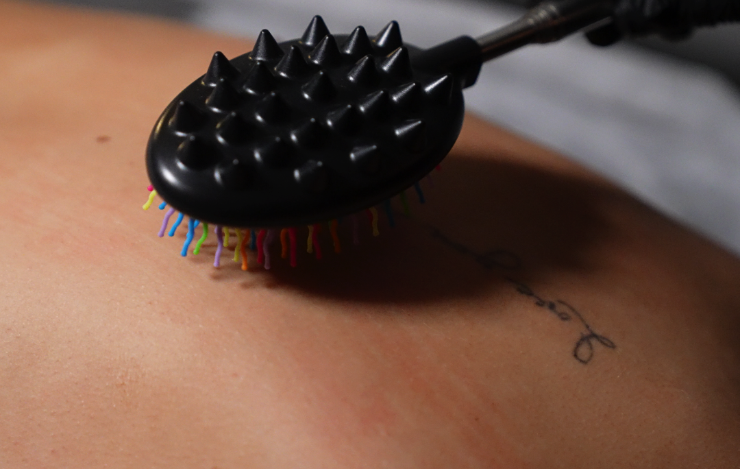 Person receiving a massage with a tool. The tool has black and colorful bristles.