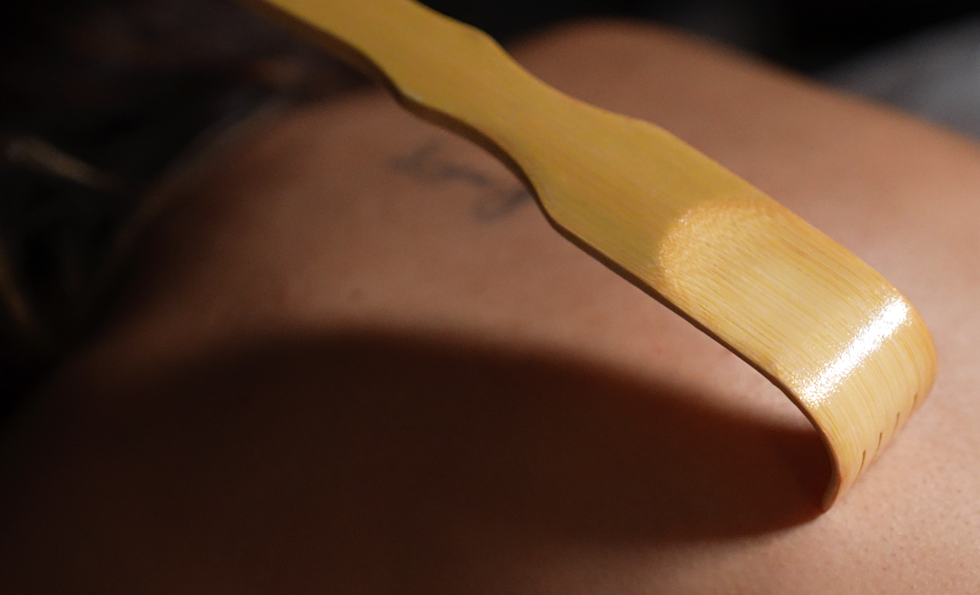 A wooden back scratcher touching a person's back; tattoo visible.