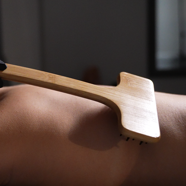 A person's back being massaged with a wooden bamboo massage tool.
