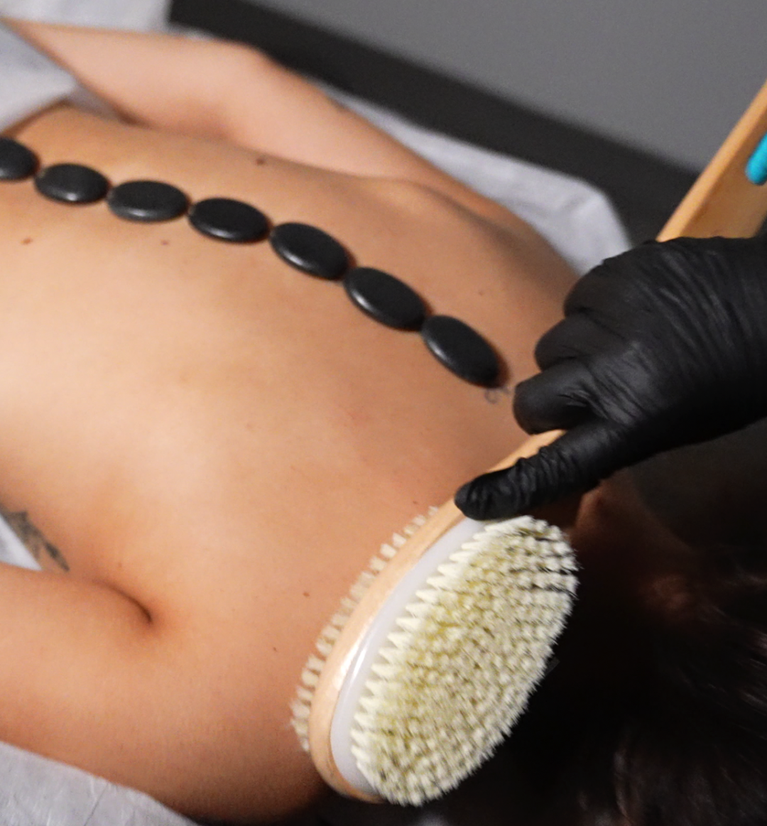 Back massage with hot stones and brush. A gloved hand works on the neck.