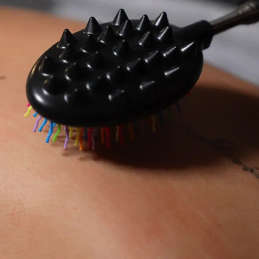 Black massage tool with spiked head on a person's back, featuring colorful bristles.