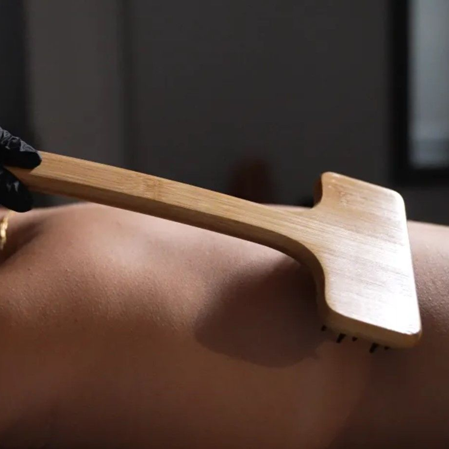 Wooden massage tool on a person's back, held by a gloved hand.