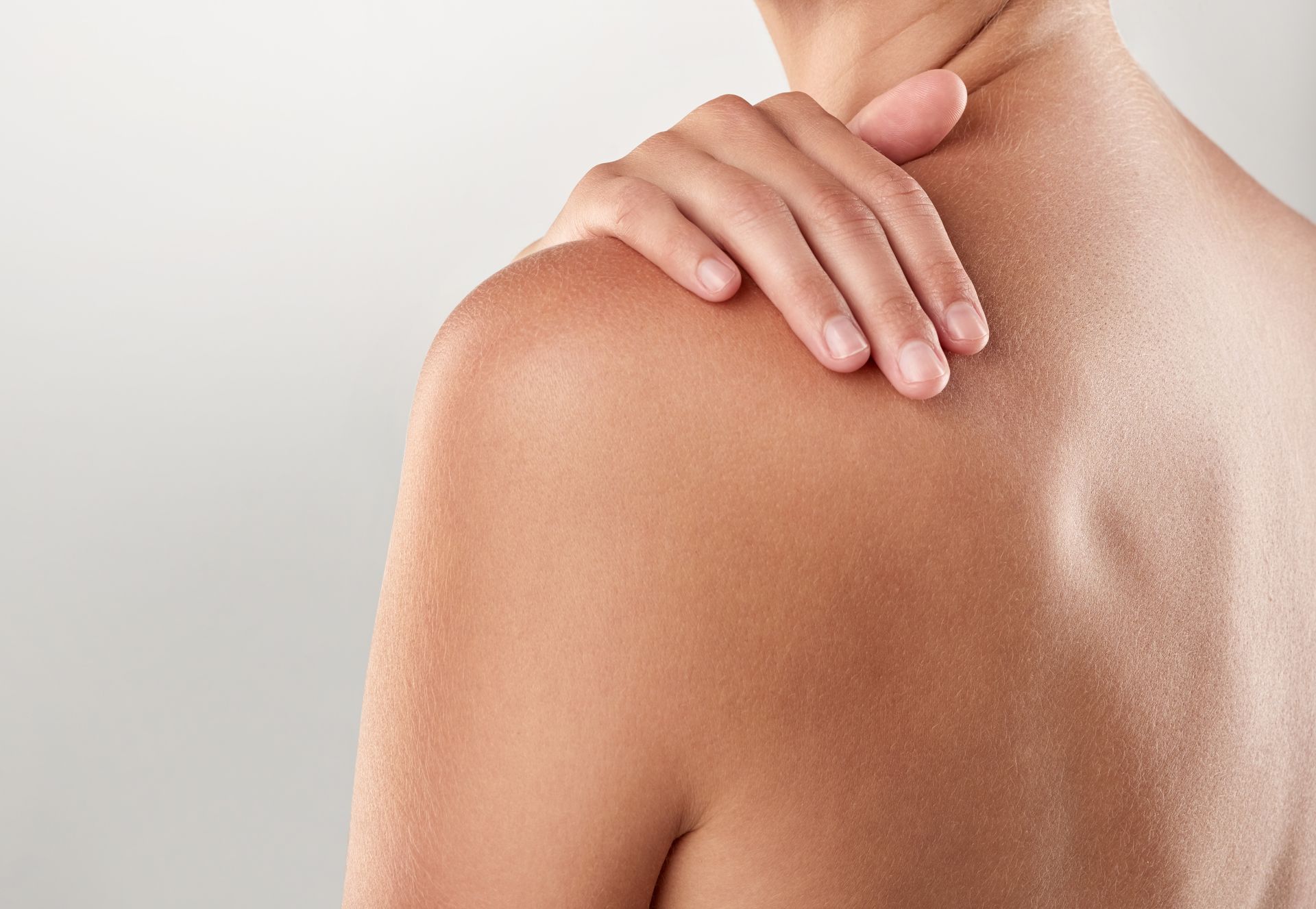A person's bare back and shoulder, hand touching shoulder, light skin.