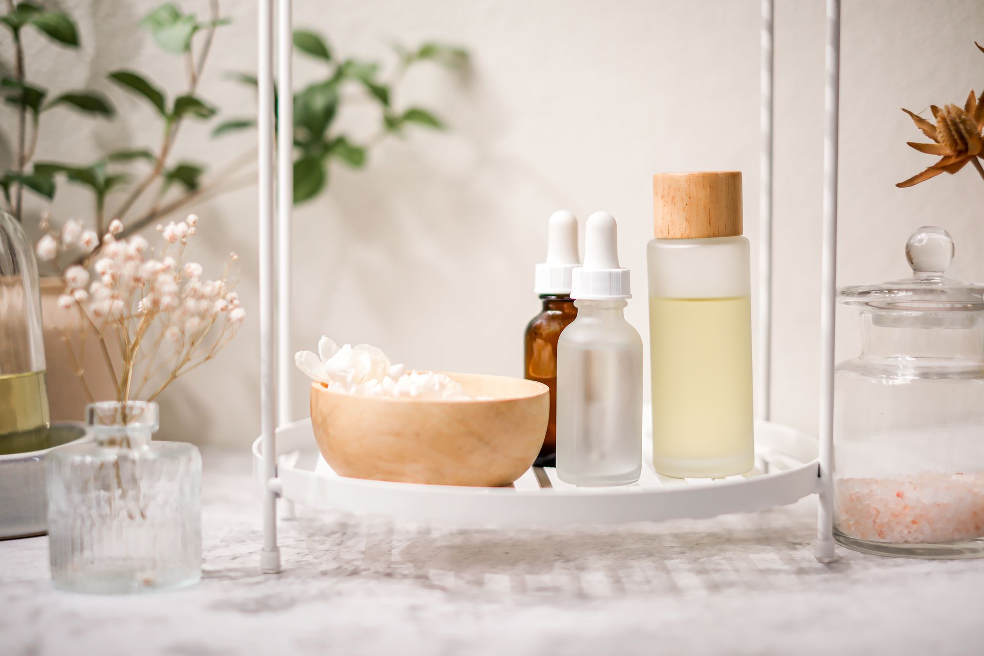 Bathroom shelf with skincare products: oils, a wood bowl, and a glass jar, all in a minimalist style.