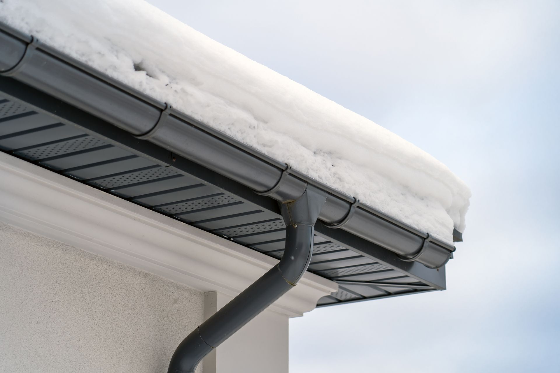 Snow-covered roof with a metal gutter and downspout designed for winter drainage. Snow-covered roof with a metal gutter and downspout designed for winter drainage.