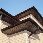 Brown roof with gutters on a beige house under a blue sky.