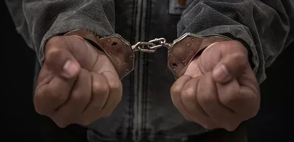 Handcuffed hands clenched into fists in a dark jacket.